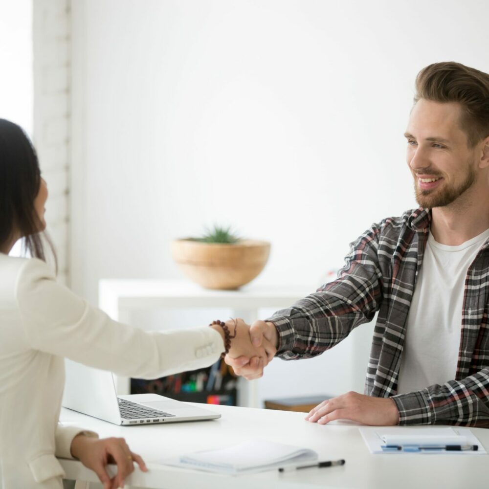Smiling millennial partners handshaking in office thanking for s